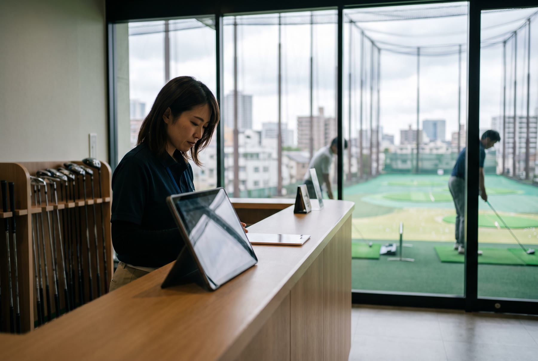練習場の受付でタブレットを見ながら予約を確認するスタッフ