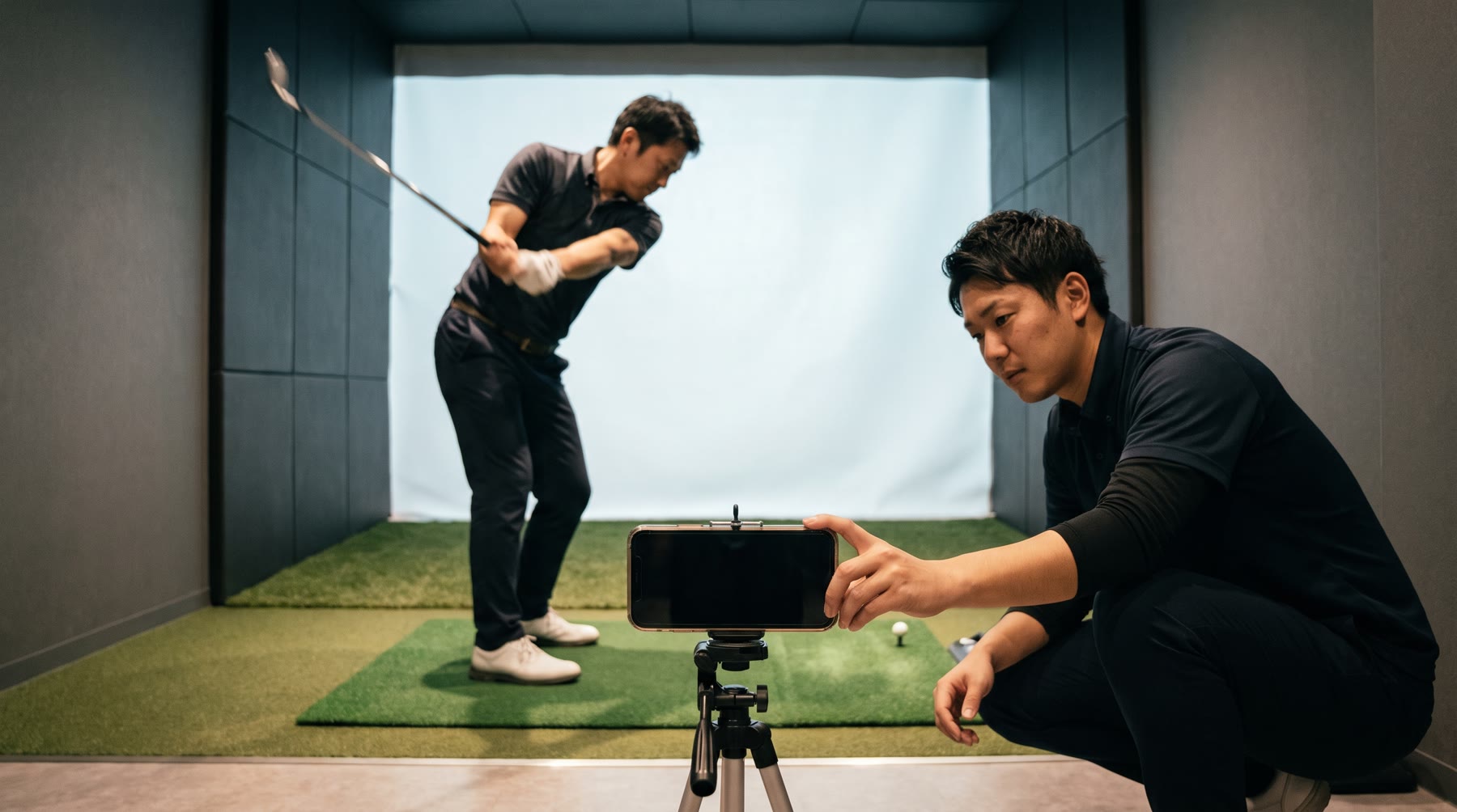 屋内シミュレータの個室で、三脚のスマホでスイングを撮影しているところ